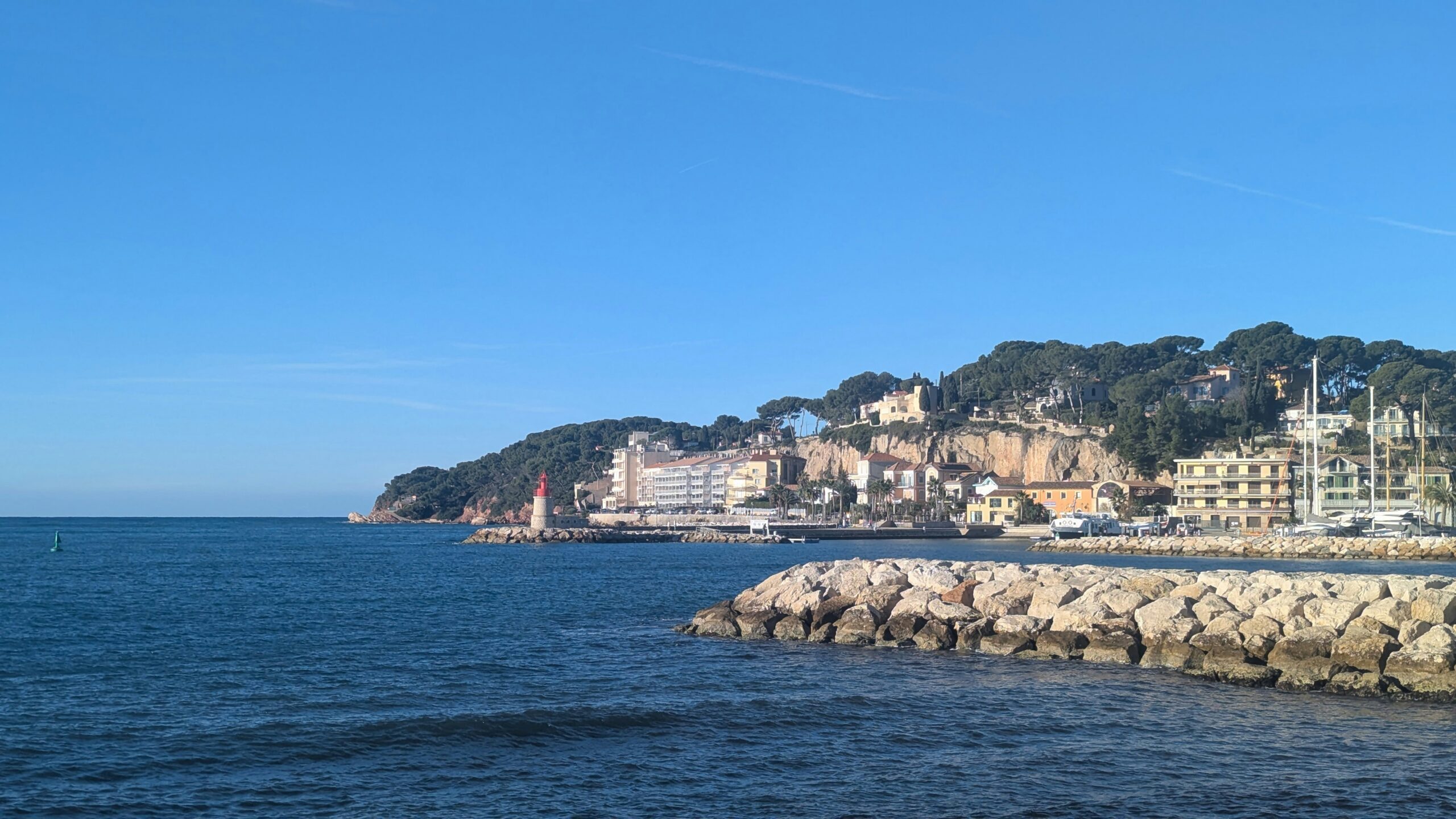 Promenade du bord de mer illuminée pour Noël sur la Côte d’Azur avec palmiers, décorations et passants en soirée